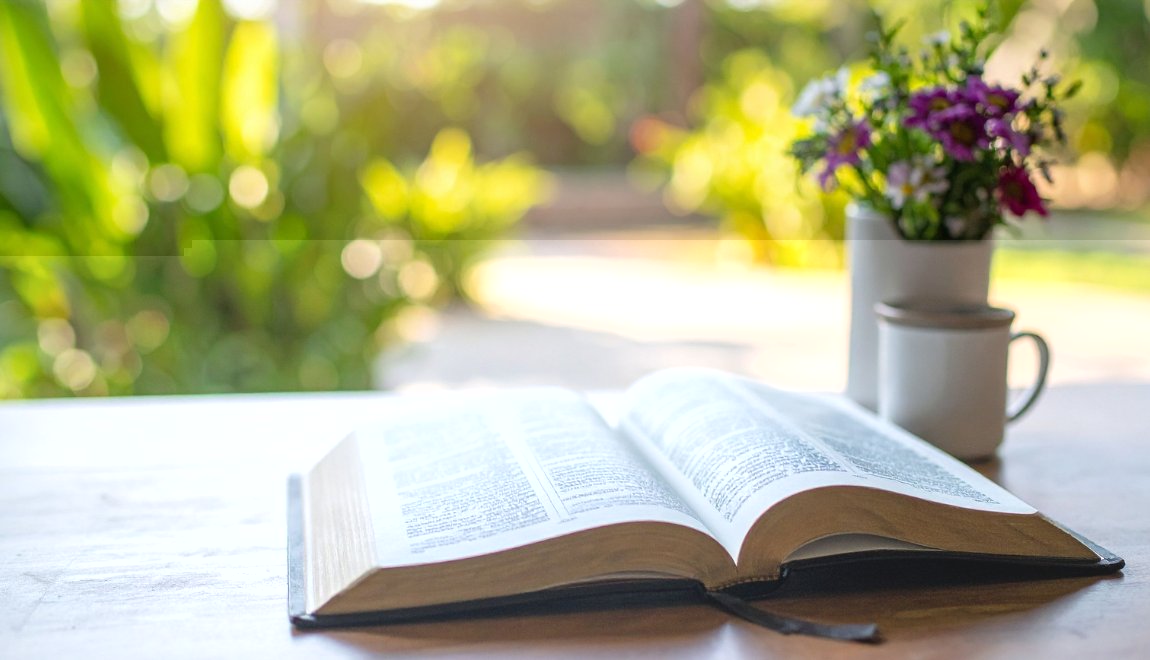 Open Bible, flowers, and a coffee mug on a table in soft morning light